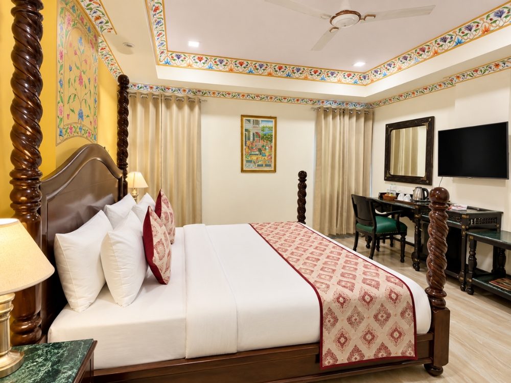 Suite Room bedroom with four-poster bed, mirror and TV console at Fort Chandragupt Hotel Jaipur